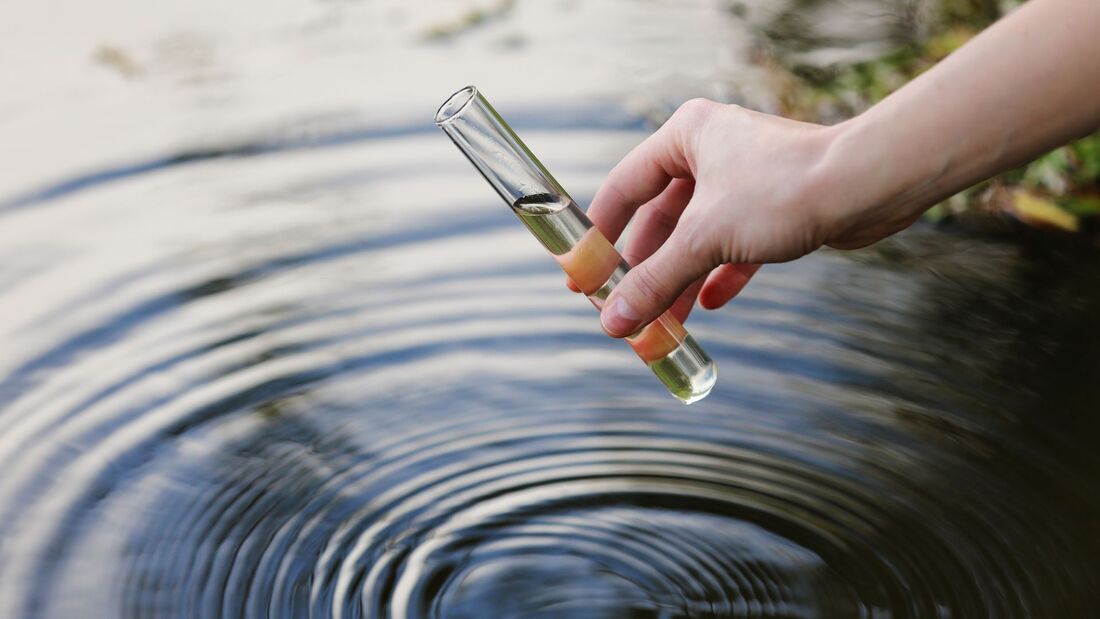 Hand holding a water sample tube over rippling water