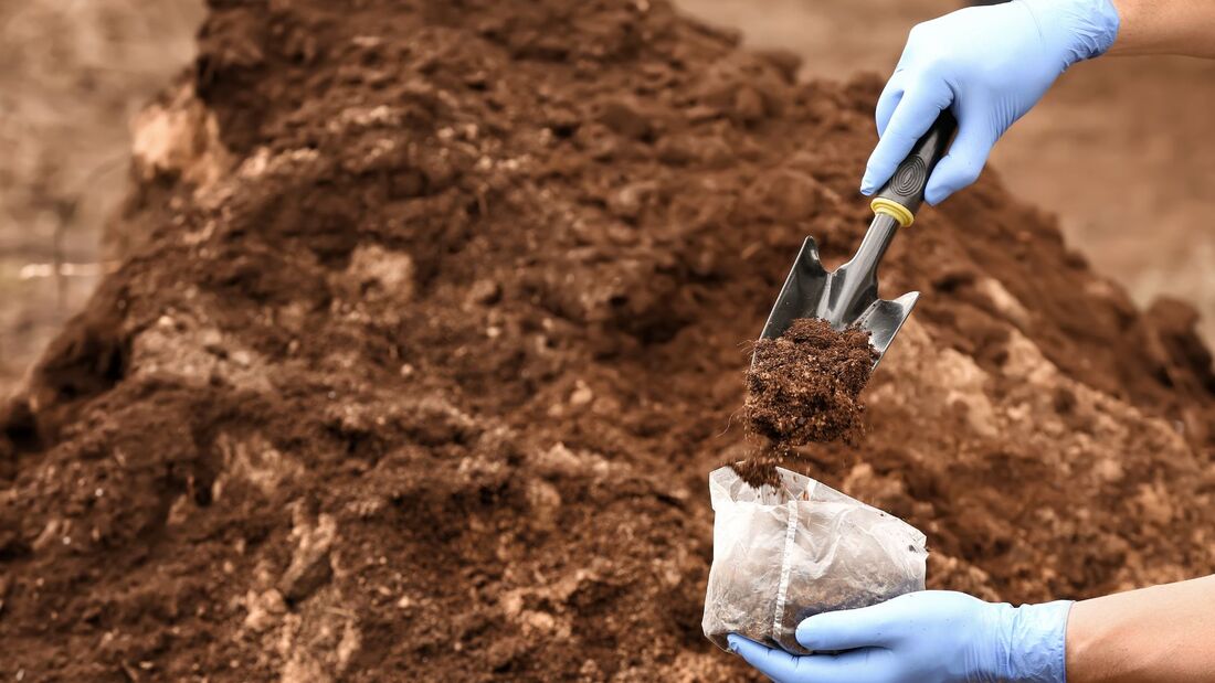 Gloved hands sampling soil into a bag